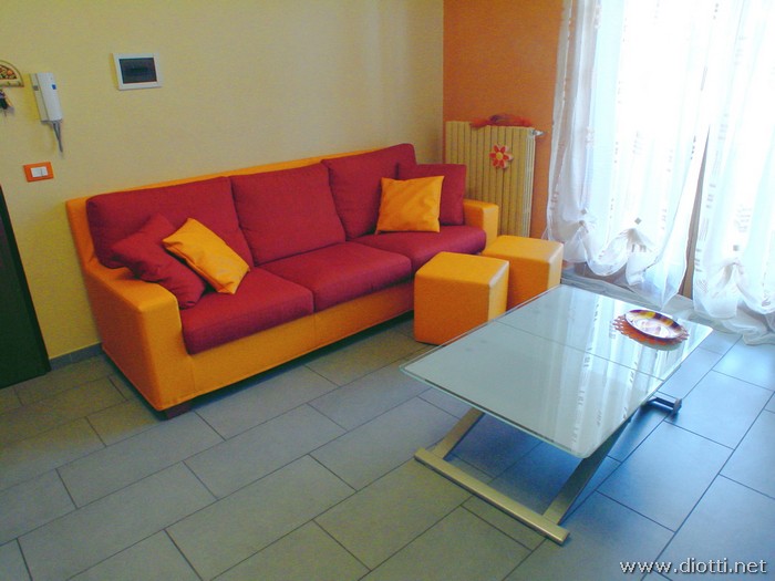 Il divano letto Canova, in versione bicolore arancio e rosso con dei pouff su misura coordinati ed il tavolino Eleven.