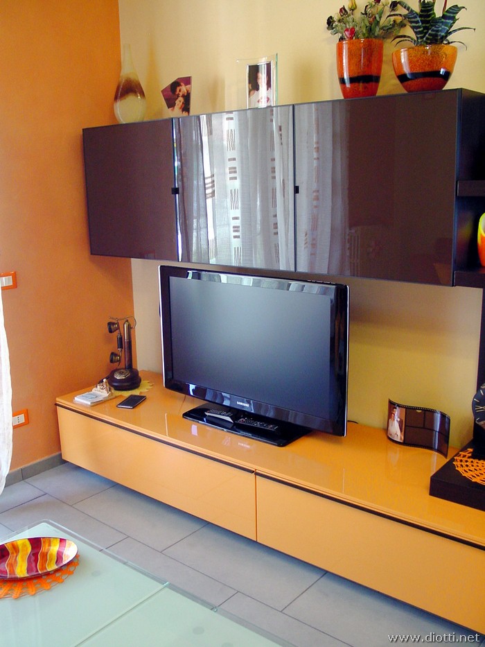 La base porta tv arancio del soggiorno Day, con i pensili in cristallo visone con telaio alluminio in tinta.