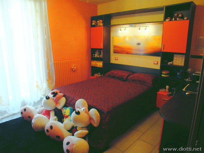 La camera matrimoniale Young in rovere tinto weng e laccato arancio opaco, con una struttura retro-letto su misura.